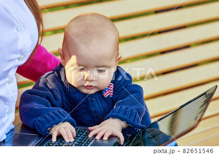 Woman sits on park bench with baby during online learning. Woman sits on park bench with baby during online learning. 82651546