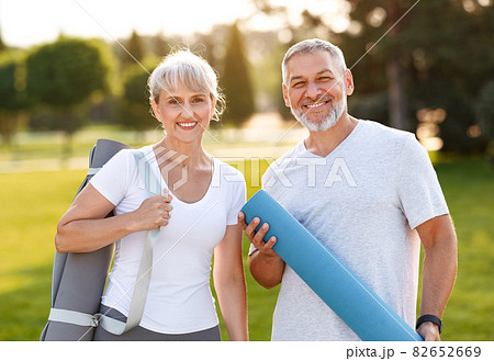 Smiling senior couple husband and wife embracing while standing at park with exercise mats 82652669