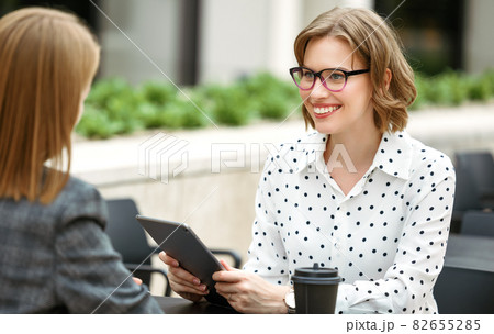 Smiling woman with digital tablet in hand discussing startup with business partner in outdoor cafe 82655285