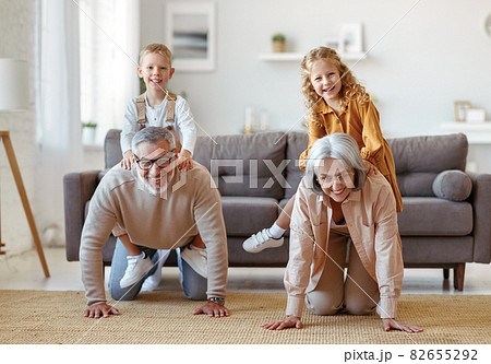 Active positive senior grandparents carrying excited little kids grandchildren on backs 82655292