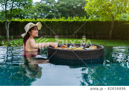 cheerful woman enjoying with floating food and champagne glass in swimming pool cheerful woman enjoying with floating food and champagne glass in swimming pool 82656896
