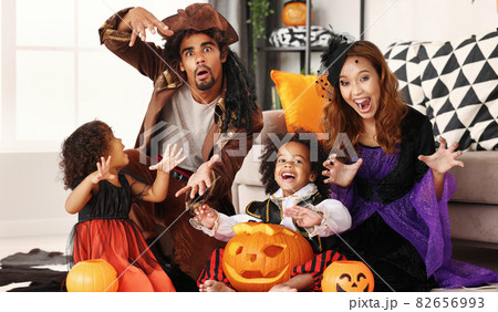 African american family in Halloween costumes making scary gesture while sitting with jack o lantern 82656993