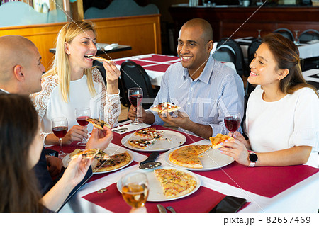 Happy friends eating delicious pizza and chatting with each other in restaurant Happy friends eating delicious pizza and chatting with each other in restaurant 82657469