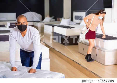 Man in protective mask selects new mattress at a furniture store 82657709
