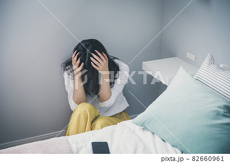 ベッド脇で頭を抱える女性 頭を抱える人 落ち込む女性の写真素材
