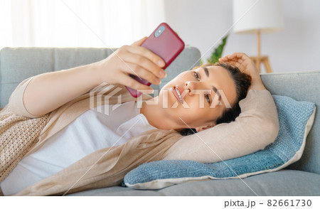 woman is using a phone sitting on a sofa woman is using a phone sitting on a sofa 82661730