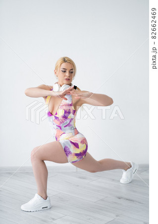 Fitness gym. Sportive woman. Home training. Healthy lifestyle. Concentrated athletic lady in colorful sportswear doing workout headphones on neck in light room interior. Fitness gym. Sportive woman. Home training. Healthy lifestyle. Concentrated athletic lady in colorful sportswear doing workout headphones on neck in light room interior. 82662469