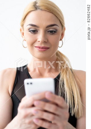 Fitness video. Inspired woman. Sport influence. Healthy body. Online conference. Beautiful happy lady in sportswear looking amazed with smartphone in hands isolated white. Fitness video. Inspired woman. Sport influence. Healthy body. Online conference. Beautiful happy lady in sportswear looking amazed with smartphone in hands isolated white. 82662482