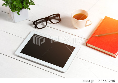 Office table desk with set of supplies, red notepad, cup, pen, tablet, glasses, flower on white background. Top view Office table desk with set of supplies, red notepad, cup, pen, tablet, glasses, flower on white background. Top view 82663296