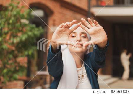 Portrait of young muslim woman wearing hijab head scarf in city while looking at camera. Closeup face of cheerful woman covered with headscarf smiling outdoor. Islamic girl outdoors. 82663888