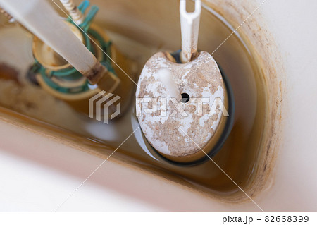 Toilet tank parts replacement. A man in orange gloves repairs the toilet tank drain. 82668399