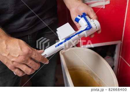 Toilet tank parts replacement. A man in orange gloves repairs the toilet tank drain. 82668400