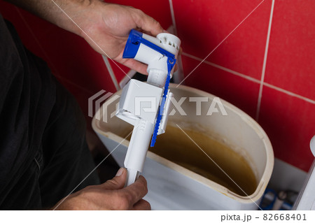 Toilet tank parts replacement. A man in orange gloves repairs the toilet tank drain. 82668401