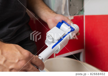 Toilet tank parts replacement. A man in orange gloves repairs the toilet tank drain. 82668402