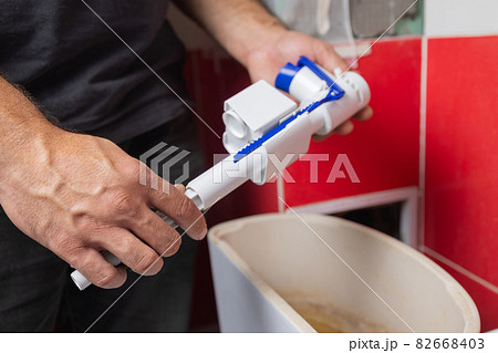 Toilet tank parts replacement. A man in orange gloves repairs the toilet tank drain. 82668403