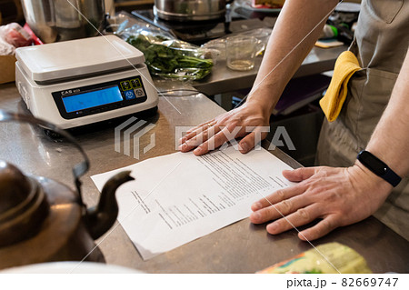 The baker looks through the recipe in the bakery on the table, dressed in an apron. The baker looks through the recipe in the bakery on the table, dressed in an apron. 82669747