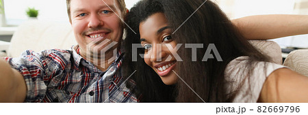Cheerful multiethnic couple in love sits in embrace in cozy living room at home 82669796