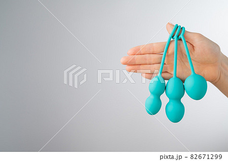 A faceless woman demonstrates a set of mint-colored vaginal balls. Girl holding a kegel trainer for training pelvic floor muscles on a white background. A faceless woman demonstrates a set of mint-colored vaginal balls. Girl holding a kegel trainer for training pelvic floor muscles on a white background. 82671299