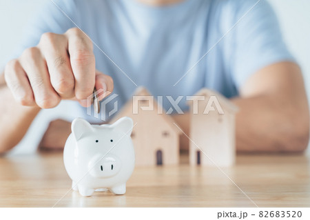 Man hand put coin into White piggy bank with wooden house on wood table. saving money for buying house, financial plan home loan concept. Man hand put coin into White piggy bank with wooden house on wood table. saving money for buying house, financial plan home loan concept. 82683520