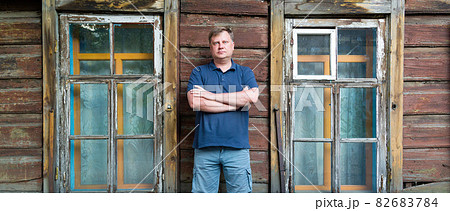 An adult man stands at a wooden abandoned building 82683784