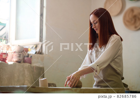 Ginger cute potter working in her workshop and looking involved Ginger cute potter working in her workshop and looking involved 82685786