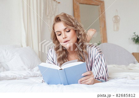 White cozy bed and a beautiful woman reading a book, concepts of home and comfort White cozy bed and a beautiful woman reading a book, concepts of home and comfort 82685812