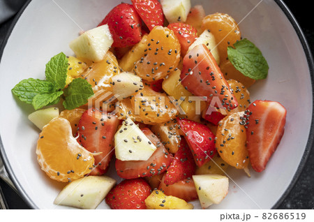 Closeup fruit salad for breakfast, mix of with fresh apple, strawberry, tangerines, pineapple and honey. Black background Closeup fruit salad for breakfast, mix of with fresh apple, strawberry, tangerines, pineapple and honey. Black background 82686519