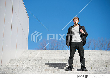 thoughtful young man sitting on steps against blue sky background 82687308