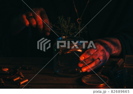 hands of sorcerer alchemist prepare a magic potion poison with herbs in flask at table 82689665