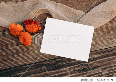 Autumn wedding still life scene. Blank greeting card mock-up. Floral composition. Orange tagetes flowers on old wooden table background. Flat lay, top view. Halloween, Dia de los Muertos holiday. Autumn wedding still life scene. Blank greeting card mock-up. Floral composition. Orange tagetes flowers on old wooden table background. Flat lay, top view. Halloween, Dia de los Muertos holiday. 82691419