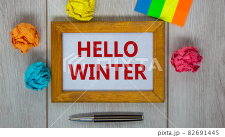 Wooden frame with inscription 'hello winter' on beautiful wooden table, colored paper, metalic pen. Concept. 82691445