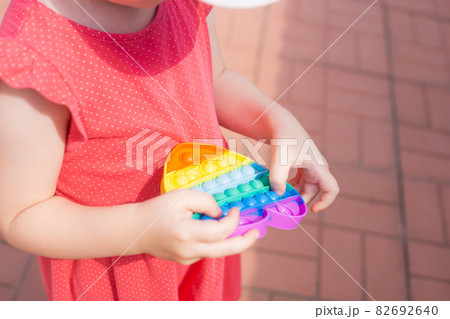 Children's hands hold a silicone toy. Kid having fun with popular simple dimple multicolored rainbow colors toy. Kids being kids LGBTQ colors Vertical. Children's hands hold a silicone toy. Kid having fun with popular simple dimple multicolored rainbow colors toy. Kids being kids LGBTQ colors Vertical. 82692640