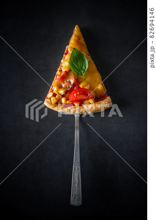 Slice of pizza with tomatoes and basil on a black background. National Italian food, pizza with tomatoes, corn, green basil and cheese on a round board. Vertical photo, place for text. Slice of pizza with tomatoes and basil on a black background. National Italian food, pizza with tomatoes, corn, green basil and cheese on a round board. Vertical photo, place for text. 82694146
