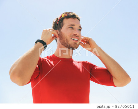 Young man putting on wireless headphone bluetooth connected to smartwatch earphones for fitness run outdoors. Happy active person wearing earbuds for exercise. Young man putting on wireless headphone bluetooth connected to smartwatch earphones for fitness run outdoors. Happy active person wearing earbuds for exercise. 82705011