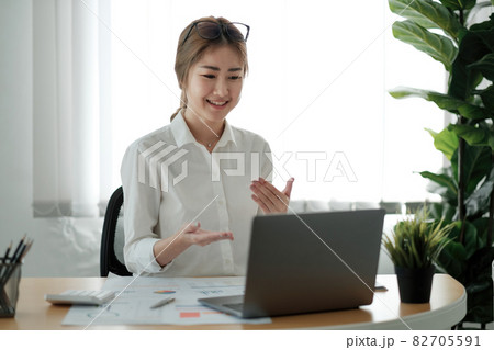 Smiling young female employee at home speak talk on video call on laptop with diverse colleagues. Asian woman worker have webcam conference or digital web team meeting or briefing with coworkers 82705591