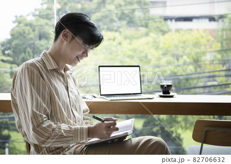 Smiling young Asian man sitting in bright office and writing new idea on notebook. 82706632