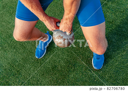 Kettlebell weightlifting man lifting crossfit weight at outdoor gym. Fitness man cross training on grass. Closeup of hands holding heavy weights for deadlift or squat workout exercise 82706780