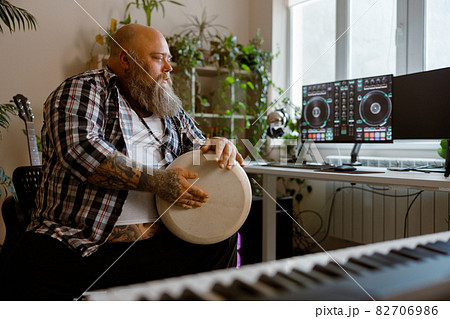 Talented man plays drum sitting at workplace with computer monitors in studio 82706986