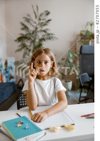 Funny little girl got idea at desk with supplies in light room Funny little girl got idea at desk with supplies in light room 82707055