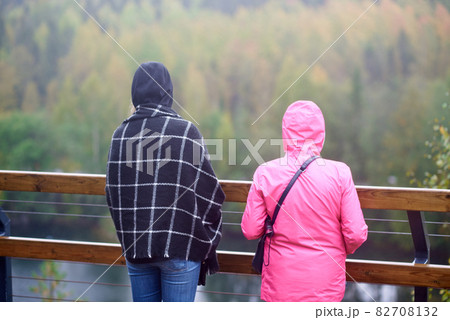 Two young women enjoy a magnificent view of the Ruskeala mountain park in Karelia. Due to the cold weather, one of the women wrapped herself in a checkered scarf, and the other put on a pink jacket. 82708132