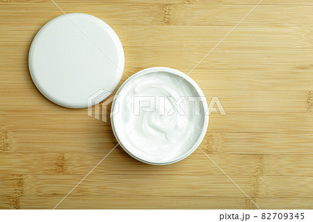 Cosmetic cream background. White cosmetic cream for skin and body in an open white jar on a wooden bamboo empty background. 82709345