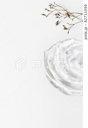 Gel texture of the emulsion on a white background. Transparent cream, small dry flowers and copy space Gel texture of the emulsion on a white background. Transparent cream, small dry flowers and copy space 82711099