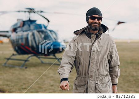 Portrait of helicopter pilot standing near vehicle in field airport Portrait of helicopter pilot standing near vehicle in field airport 82712335