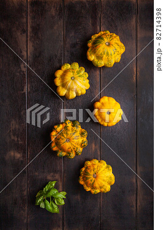 Yellow patissons or squash and a basil leaf on a brown wooden background. Yellow patissons or squash and a basil leaf on a brown wooden background. 82714398