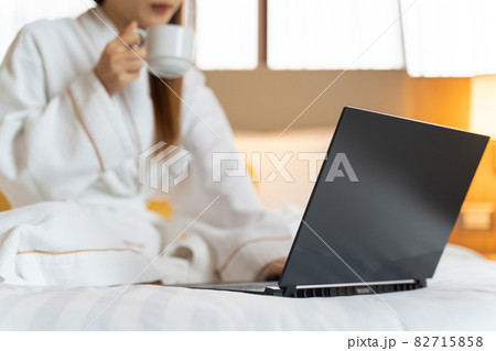 Portrait of Asian woman wearing bathrobe using a laptop for video call while have a morning coffee on bed in bedroom 82715858