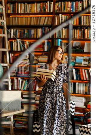 Back to school library concept. Student girl holding book on her hands on background of bookshelves in the library. Education and school concept. 82716276