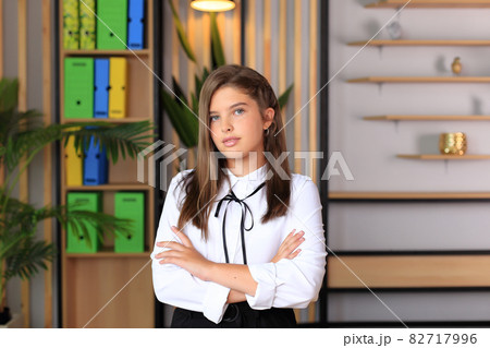 Young beautiful girl in office style looks at the camera. A teenager in school clothes in the office. Young teacher in a school class. Business girl in the office 82717996