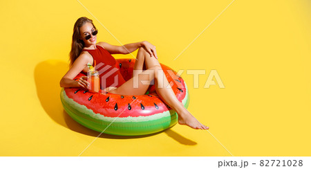 Beautiful young woman sits in inflatable ring while holds coctail isolated on color background Beautiful young woman sits in inflatable ring while holds coctail isolated on color background 82721028