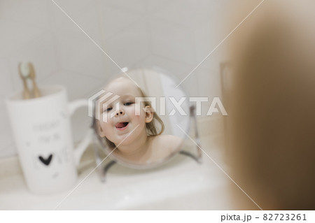 reflection in the mirror of a little funny girl washing hands and face in the bathroom 82723261