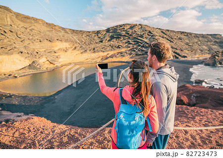 Hikers taking phone photo hiking in Spain mountain landscape . Travel couple tourists on summer hike with backpack. Woman, caucasian man hikers happy in Lanzarote National Park, Spain, Europe 82723473